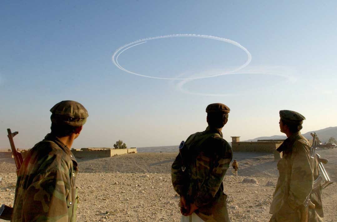 2002年9月15日，阿富汗，反塔利班士兵看着美国轰炸机在阿富汗托拉博拉地区飞过后留下的烟迹。摄：Chris Hondros/Getty