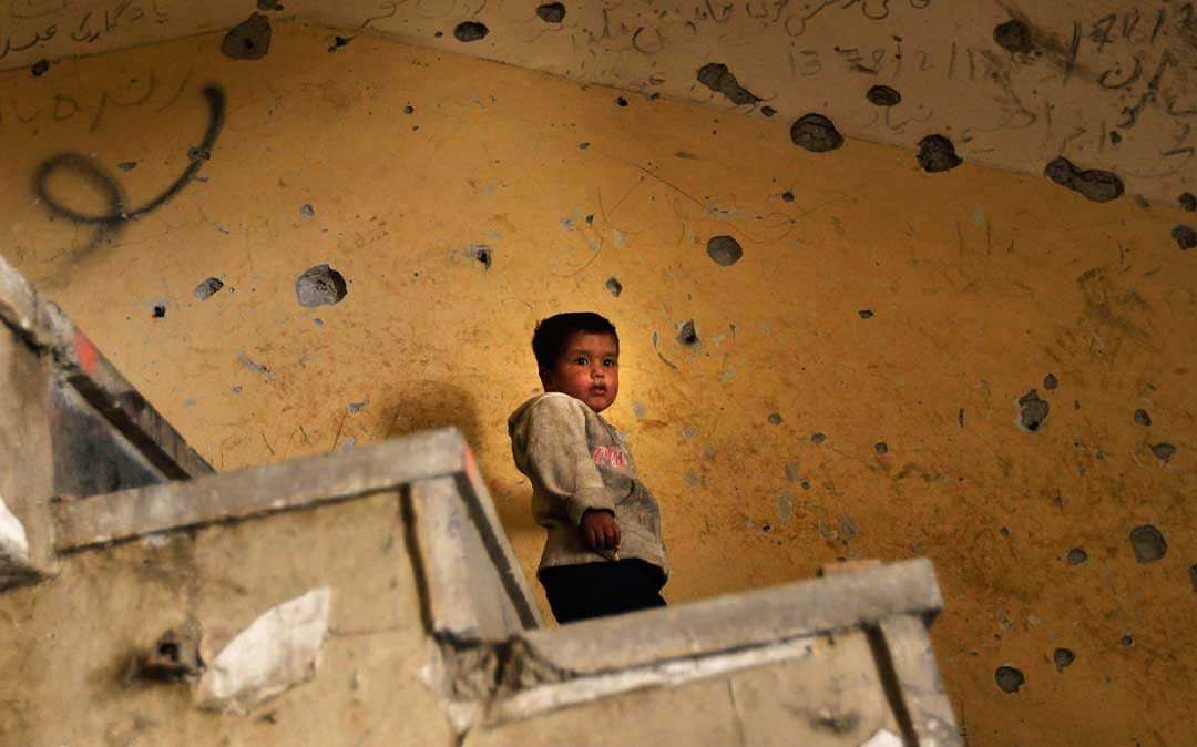 2010年10月21日，阿富汗喀布尔，一名阿富汗男孩站在充满弹孔的墙前。摄：Chris Hondros/Getty