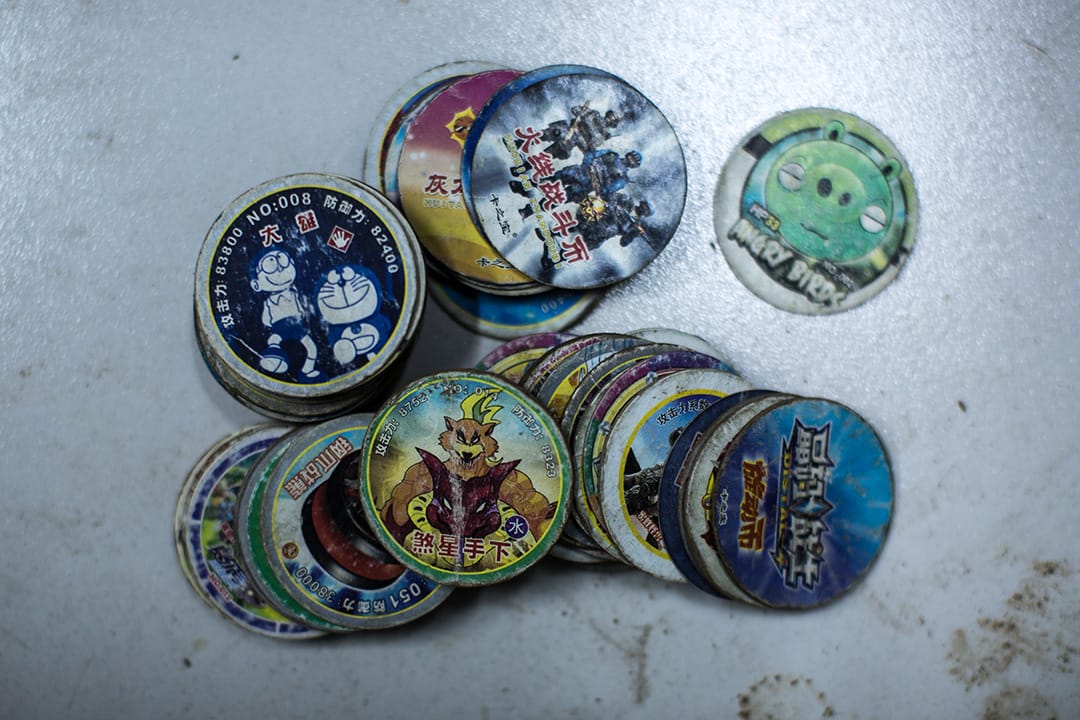 河會小學受災安置點，11 歲的程明哲從 7 歲開始玩這種圓型的「牌兒」，家裡就有一整個鞋盒的「牌兒」，結果被洪水來時被沖走了。到安置點後程明哲問爸爸要了五毛錢，重新買了一副「牌兒」和其它小朋友玩。