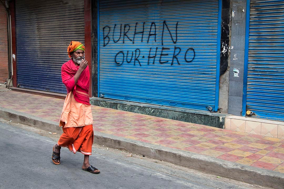 一名僧侣走过一家门外喷有支持Burhan Wani口号的店铺。