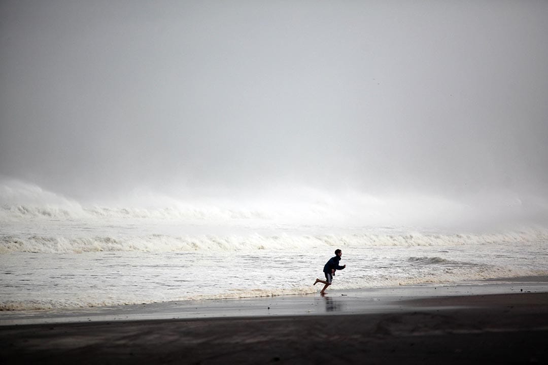 纽约,一个小孩在台风来临前的沙滩上逐浪。