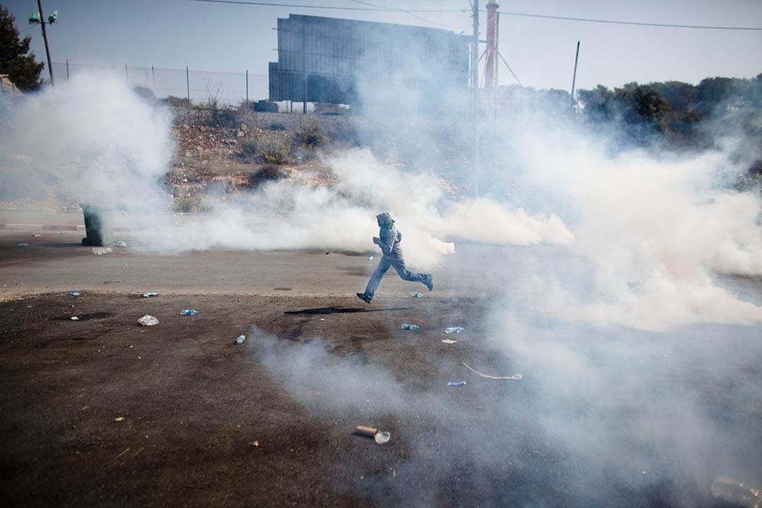 以色列,以色列防暴警察发射催泪弹,一名男生在烟雾中逃跑。