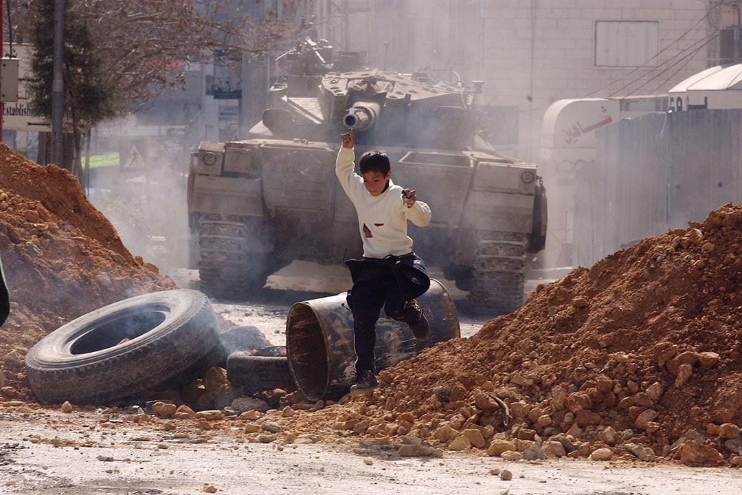 巴勒斯坦,一名男孩向坦克车投掷石头后,逃跑寻找掩护。