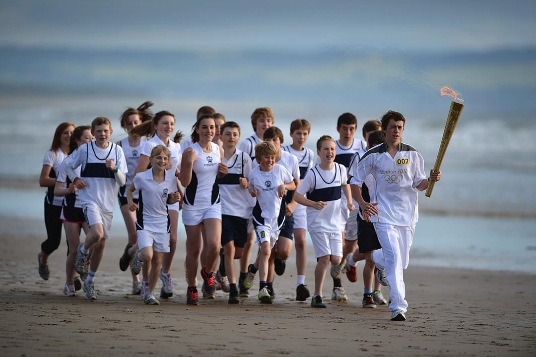 2012年6月13日,苏格兰,奥运火炬手Joseph Forrest带领着马德拉斯学校的学生沿着海滩跑步。