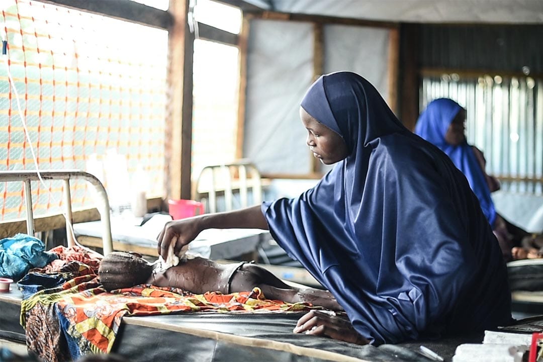 2016年8月，尼日利亞博諾州(Borno State, Nigeria)，在丹博阿(Damboa)一間綜合醫院的隔離病房內，一個母親把沾濕了的毛巾放在女兒的身體上，希望幫助她退燒。她的女兒患上麻疹並出現併發症，正接受治療。病情最嚴重的個案會獲轉介至兩小時車程外、位於比烏(Biu)的醫院作進一步治療。