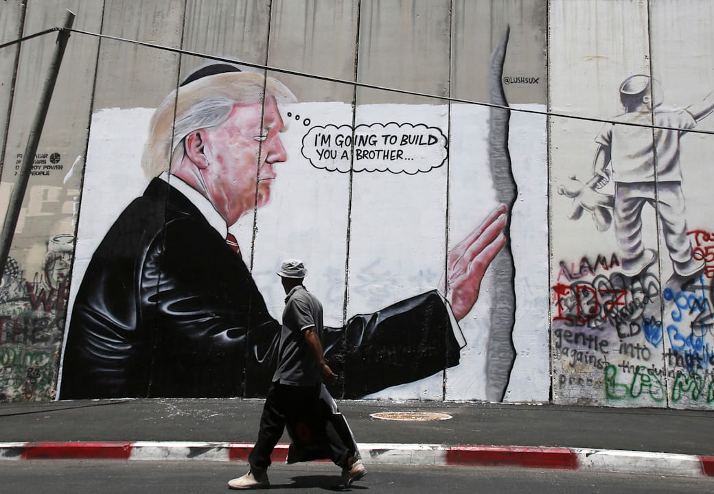 2017年8月4日，在巴勒斯坦的伯利恒，一名途人行经一幅画了特朗普在以巴边境的隔离墙的情况，讽刺特朗普的墨西哥围墙政策。