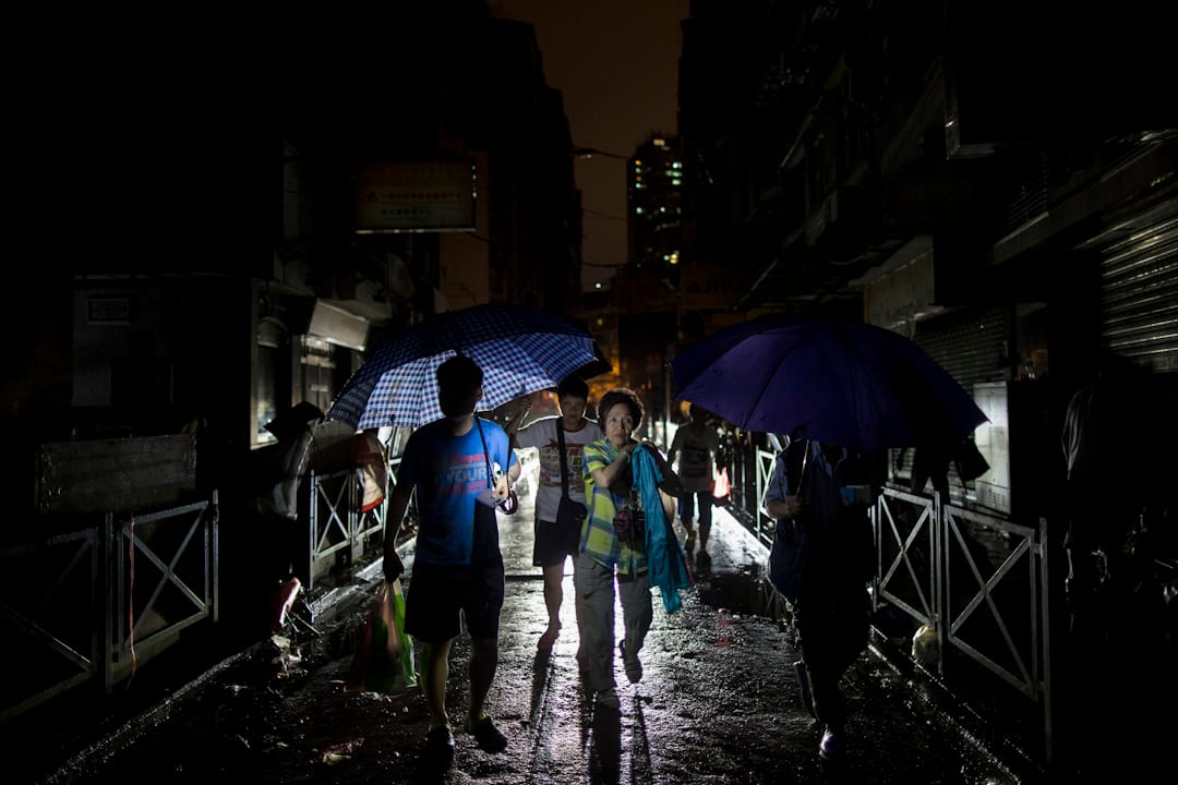 入夜後，澳門的街道仍然漆黑，還下起雨來，市民撐著傘，靠走過的車輛的車頭燈照明，橫越街道。