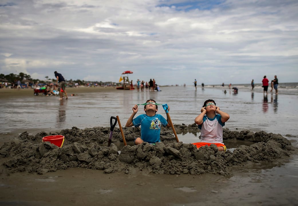 2017年8月21日，美国南卡罗来纳州的希尔顿黑德岛，一对兄弟坐在海滩上一边玩泥沙一边看日蚀。
