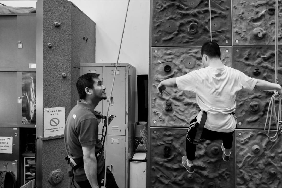 學了6個月攀石的洵詣攀到牆頂後,教練 Eric 把他慢慢放下來。