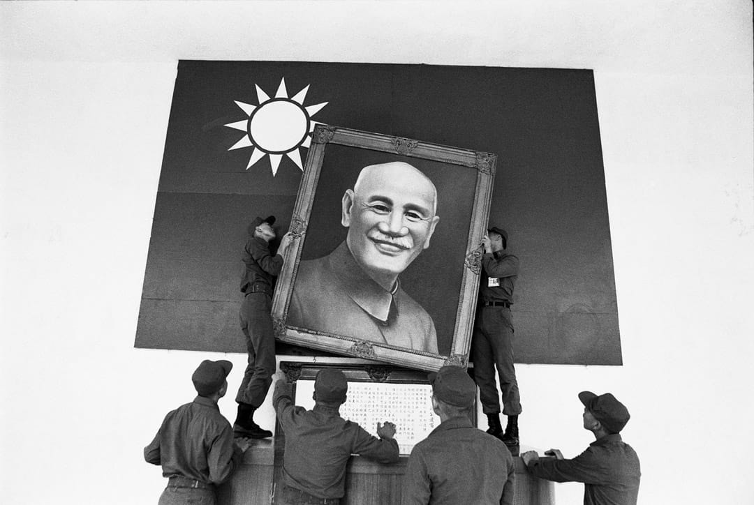 一群在佈置司令台的阿兵哥,在國旗前掛上蔣介石遺像。