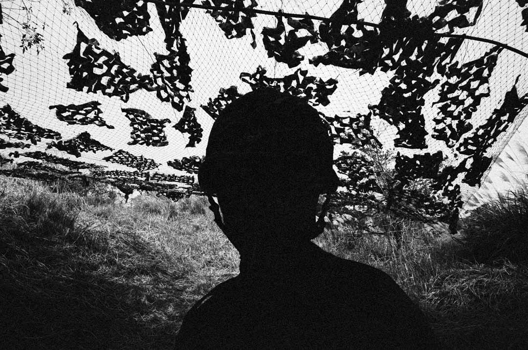 野外演習的偽裝網下,一位戴着鋼盔阿兵哥的剪影。