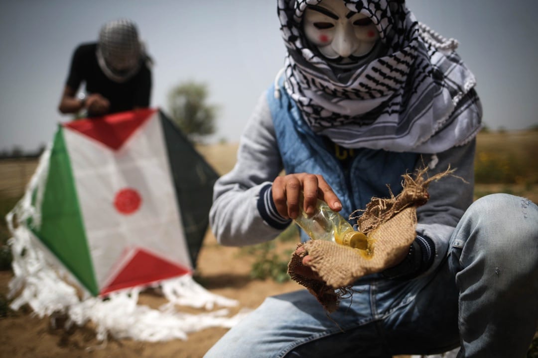 2018年4月20日,加沙地区,两名巴勒斯坦示威者整准备用风筝将土制燃烧弹飞越以色列边防部队投掷到以色列领土上。由巴勒斯坦人发起,计划持续至5月15日的“回归大游行(The Great March of Return)”步入第四周,巴勒斯坦示威者不断用创新的方式攻击以方边防部队。