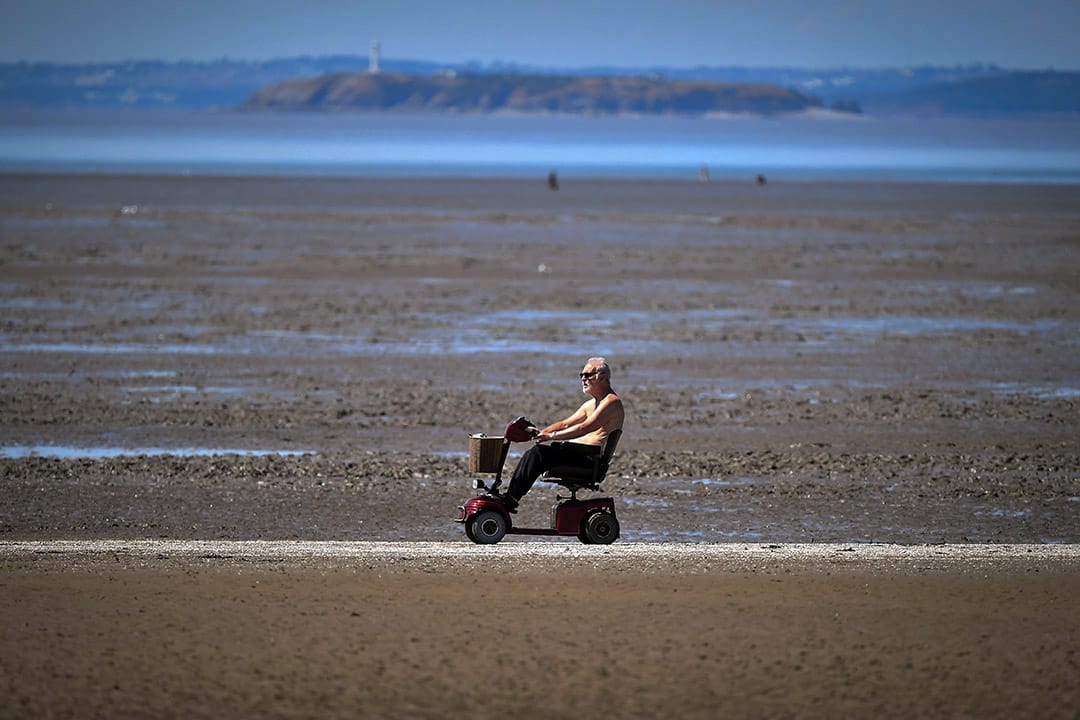 2018年7月15日,英国西部城镇滨海韦斯顿,一名男子坐著电动代步车经过沙滩。