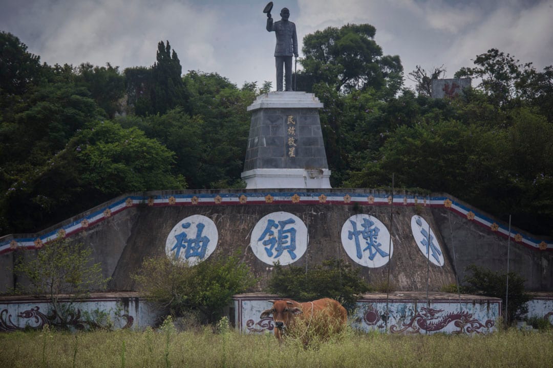 小金门岛上竖立了一个蒋介石像，空地被野草和牛占据。