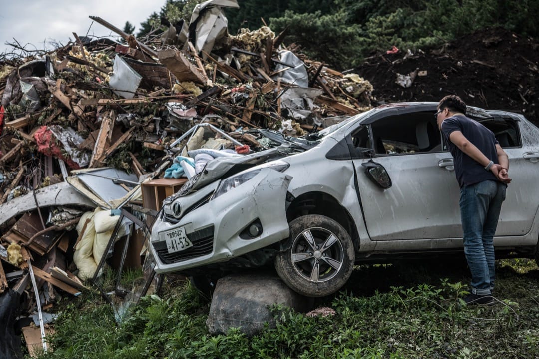 2018年9月8日，日本北海道厚真町，地震引發山泥傾瀉，壓毀多間房屋及多輛汽車，一名途人走到汽車前看汽車的損毀情況。 