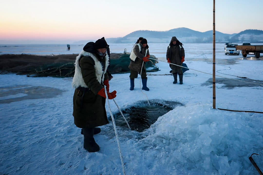 渔民在冰上钻开一个洞,将渔网放入水中。