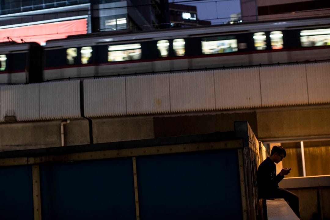 一名少年在裕民坊的平台玩手机,一列地铁在后面的一段架空铁路驶过。