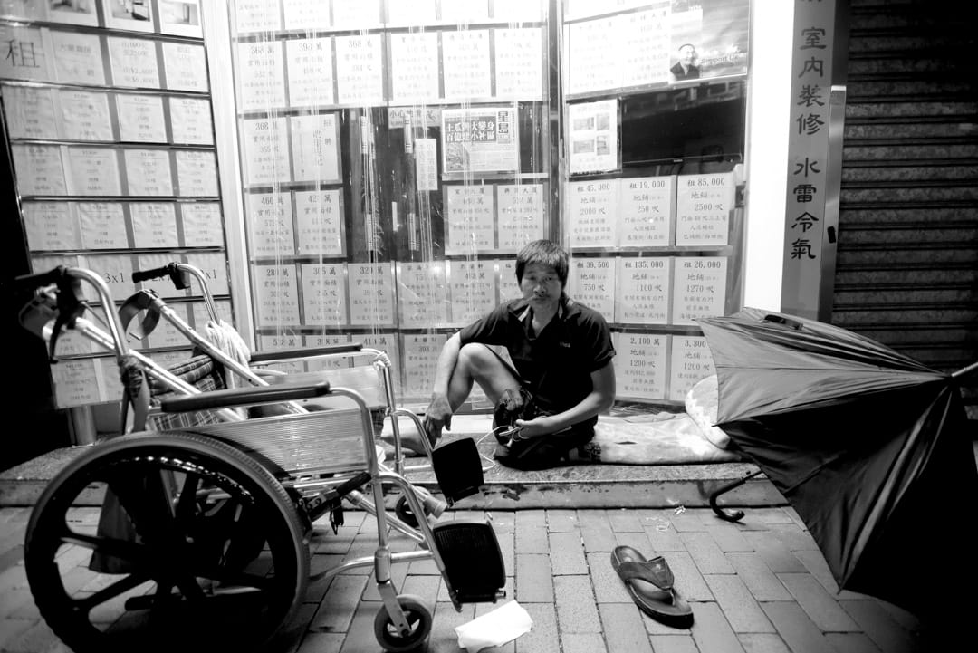 坐轮椅的发哥，因为租唔起地产舖门口广告的4500蚊月租有电梯的㓥房，他唯有瞓在地产舖门前“发个好梦”。