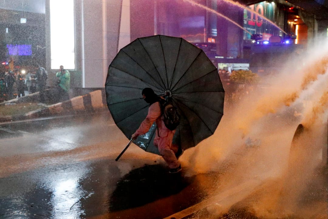 2020年10月16日泰国曼谷,一场反政府抗议活动中一名男子躲在伞下。