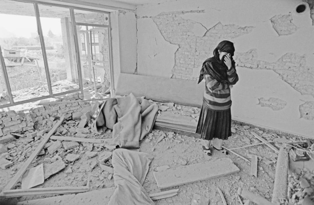 一名穿头巾的女子站在一间破烂的房间里。