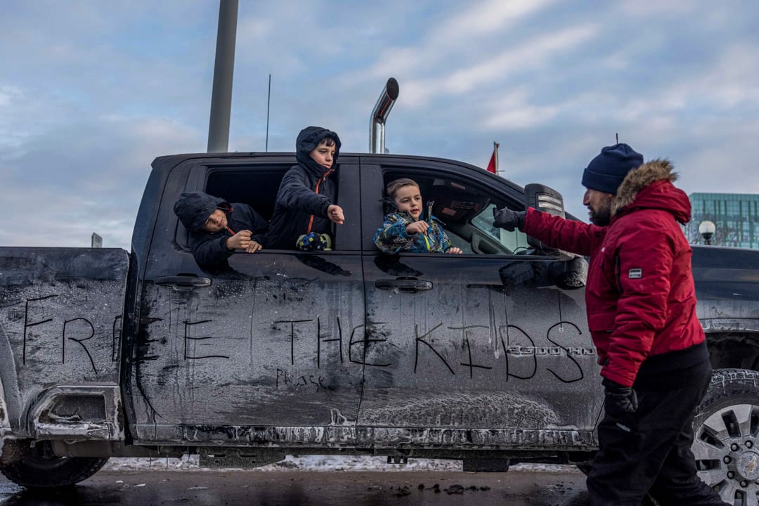 2022年1月30日,加拿大首都渥太华,三名小孩从一辆停泊在路边的车上向一位反疫苗示威者打招呼。