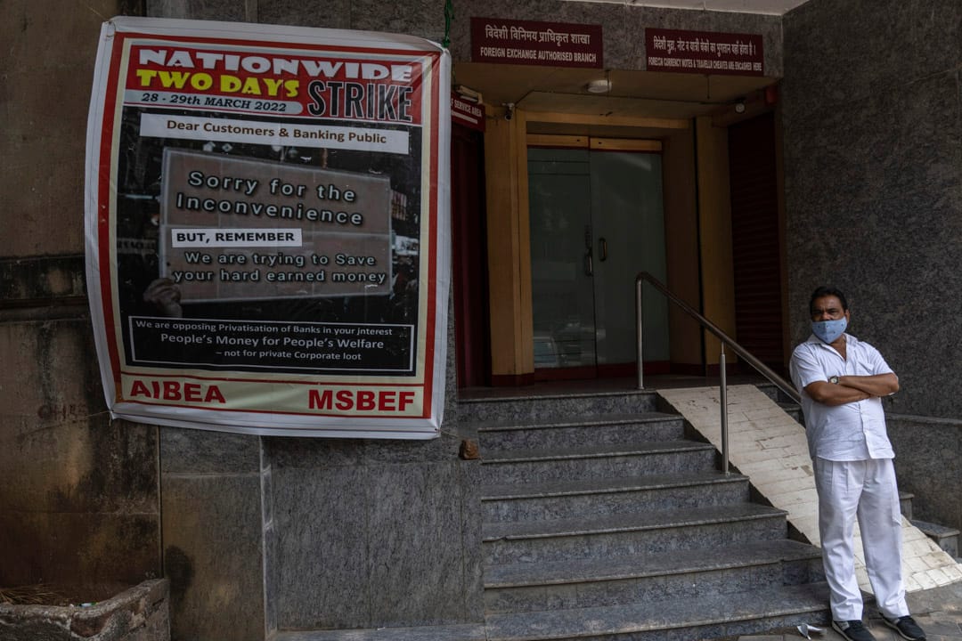 2022年3月28日,印度城市孟買,一名男子在銀行外面站著,門外有一張海報就員工罷工對前來的顧客造成不變致歉,稱罷工是為了保障顧客們的血汗錢。