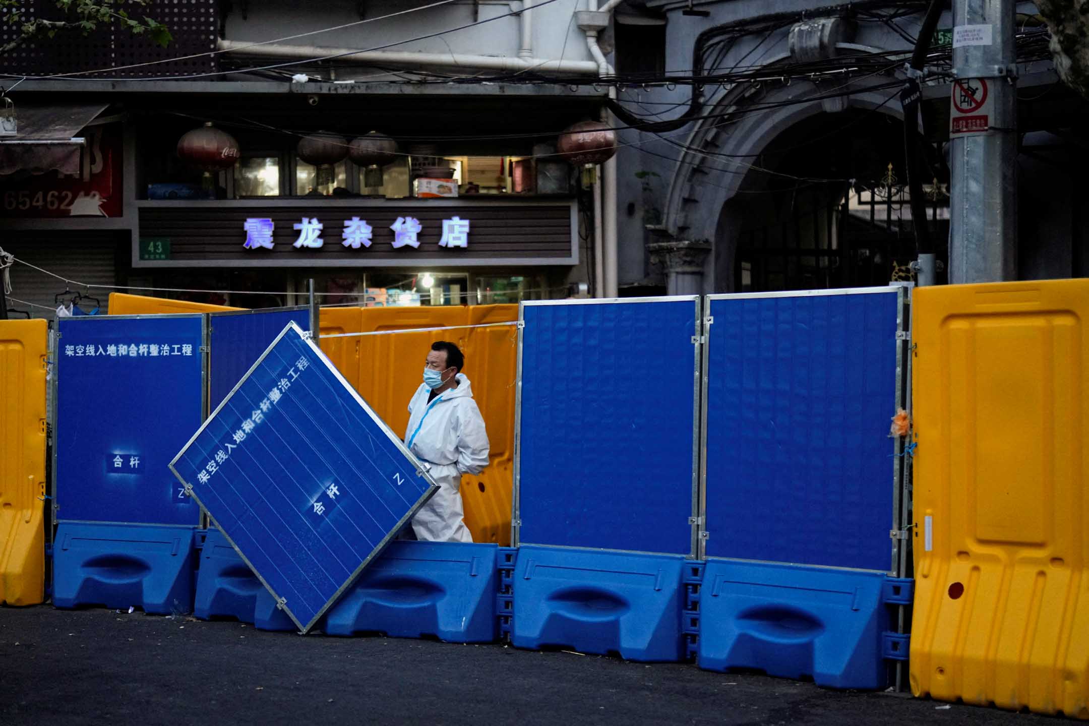2022年4月11日,中國上海,因疫情被封鎖的社區,一名身穿防護衣的工作人員在封閉區的路障旁。