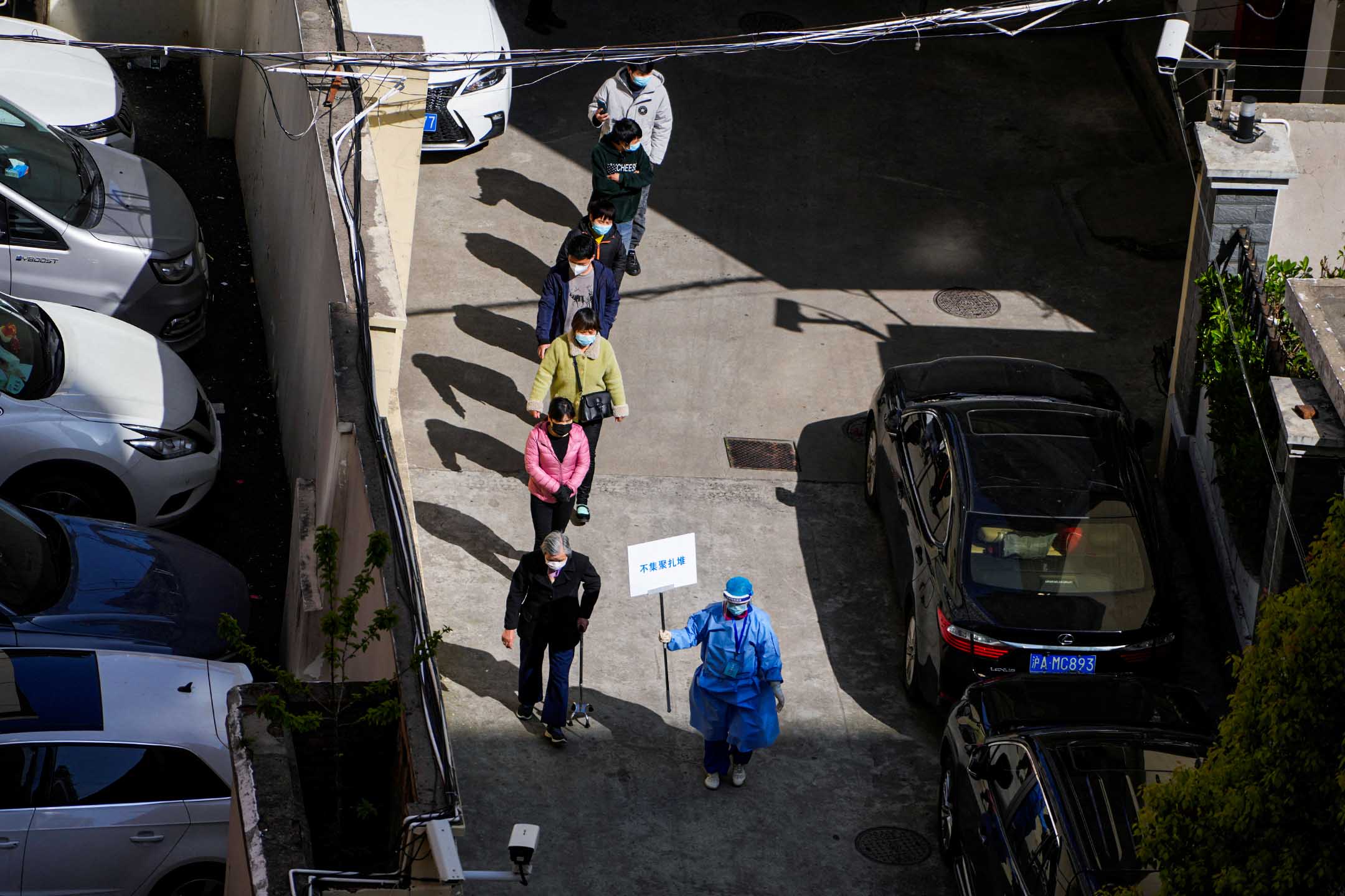 2022年4月4日,中國上海,封城期間,一名身穿防護衣的工作人員指導居民排隊進行核酸檢測。