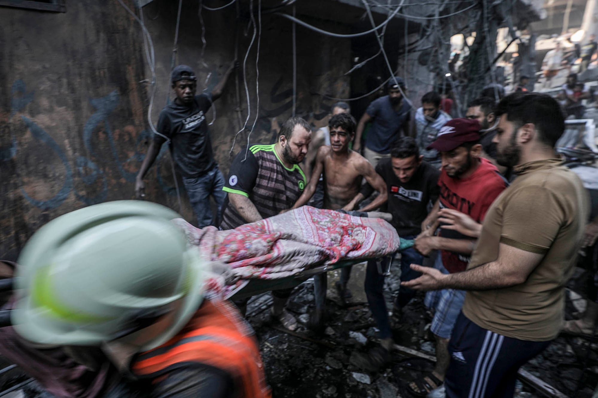 2023年10月12日，加沙走廊西部沙蒂難民營遭以色列火箭襲擊，一名傷者從現場被眾人抬出。攝：Haitham Imad/EPA/達志影像