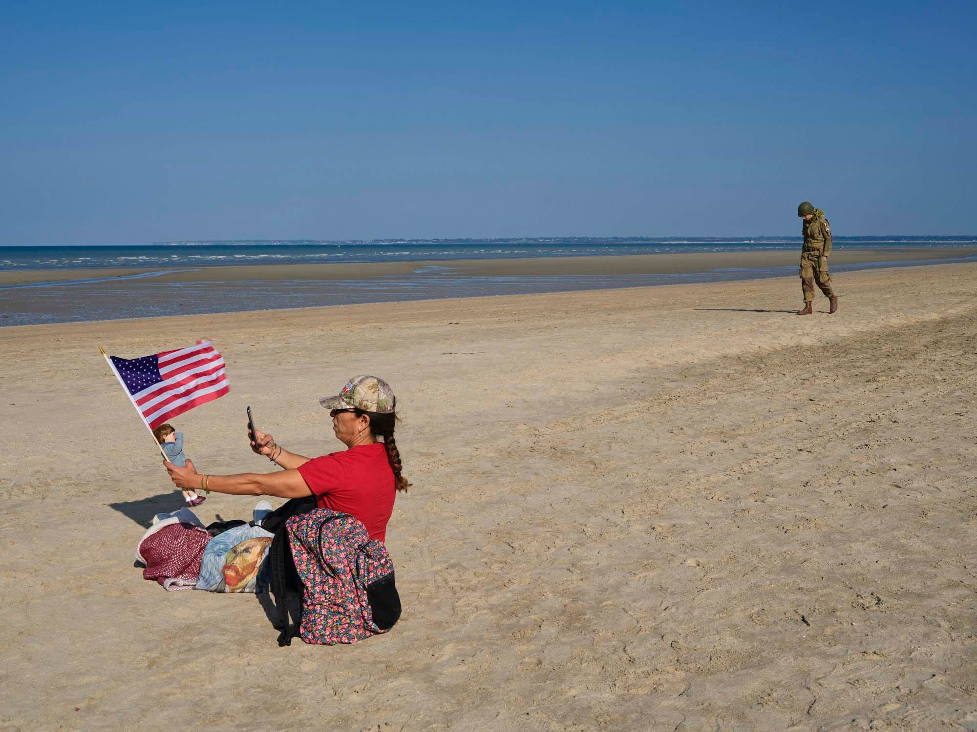 猶他海灘，一位女士在拍攝一支美國國旗時,一個穿着美國軍服的軍迷走過海灘。攝影：Vincent Yu